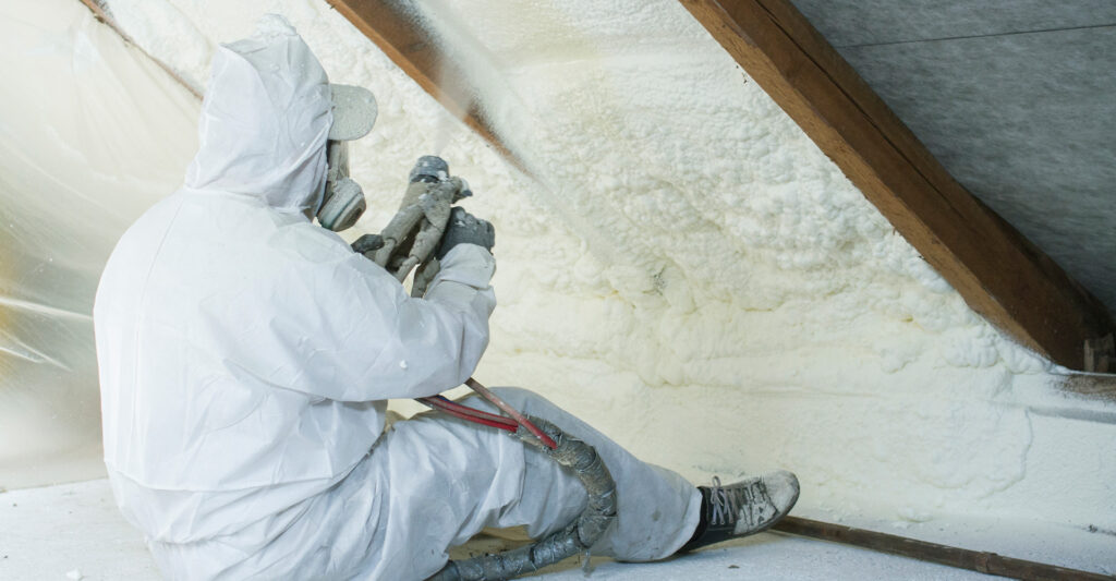 worker applying spray foam insulation in attic